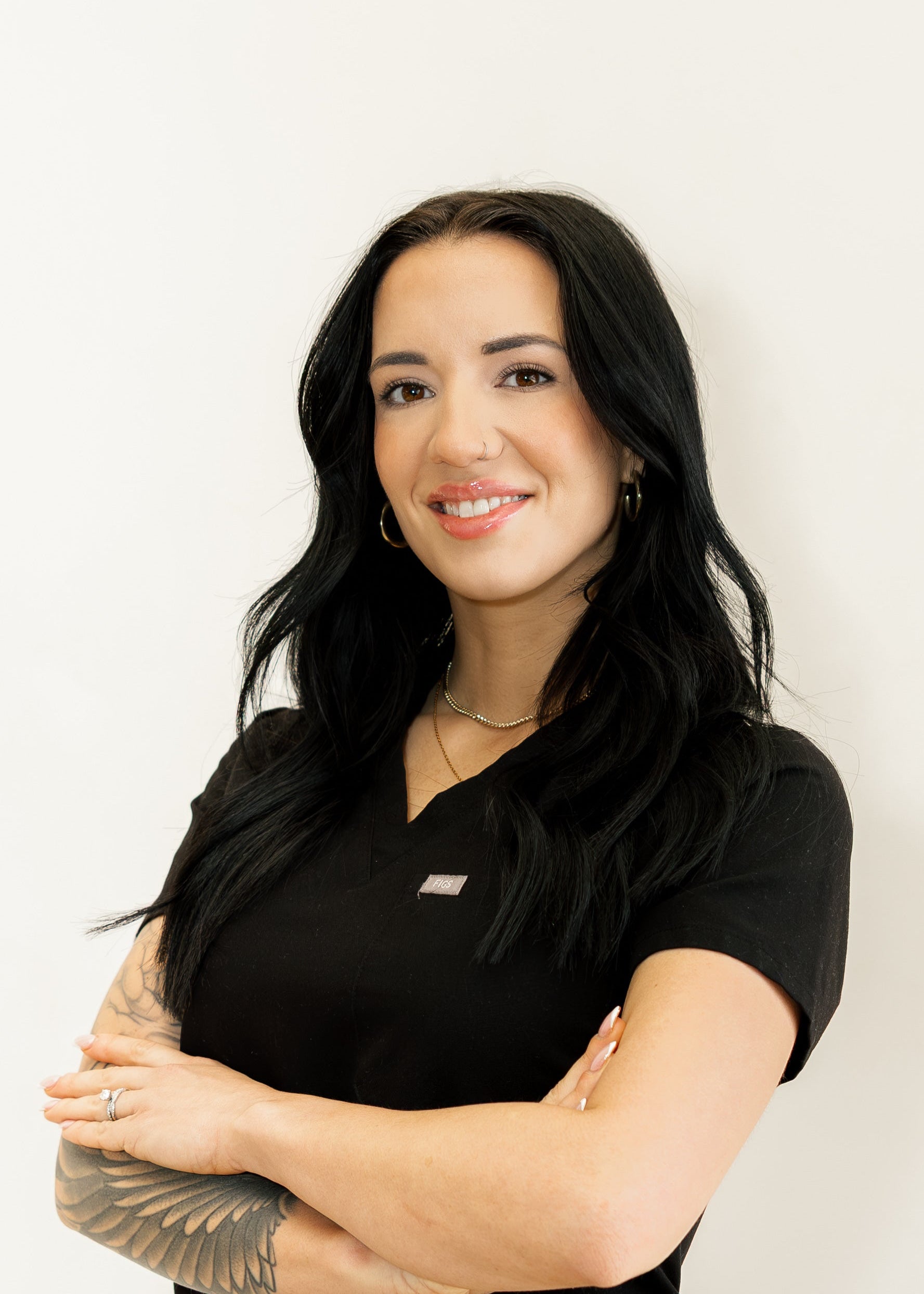 Woman with black hair and tattoos wearing a black shirt against a white background