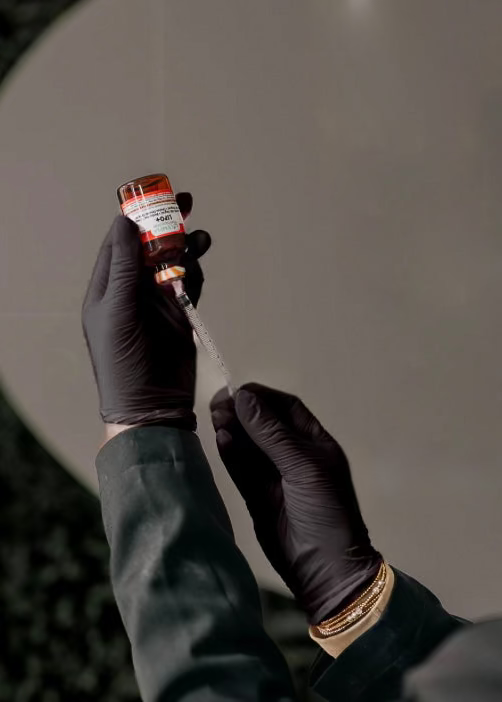 Person wearing black gloves holding a small bottle with a dropper against a neutral background